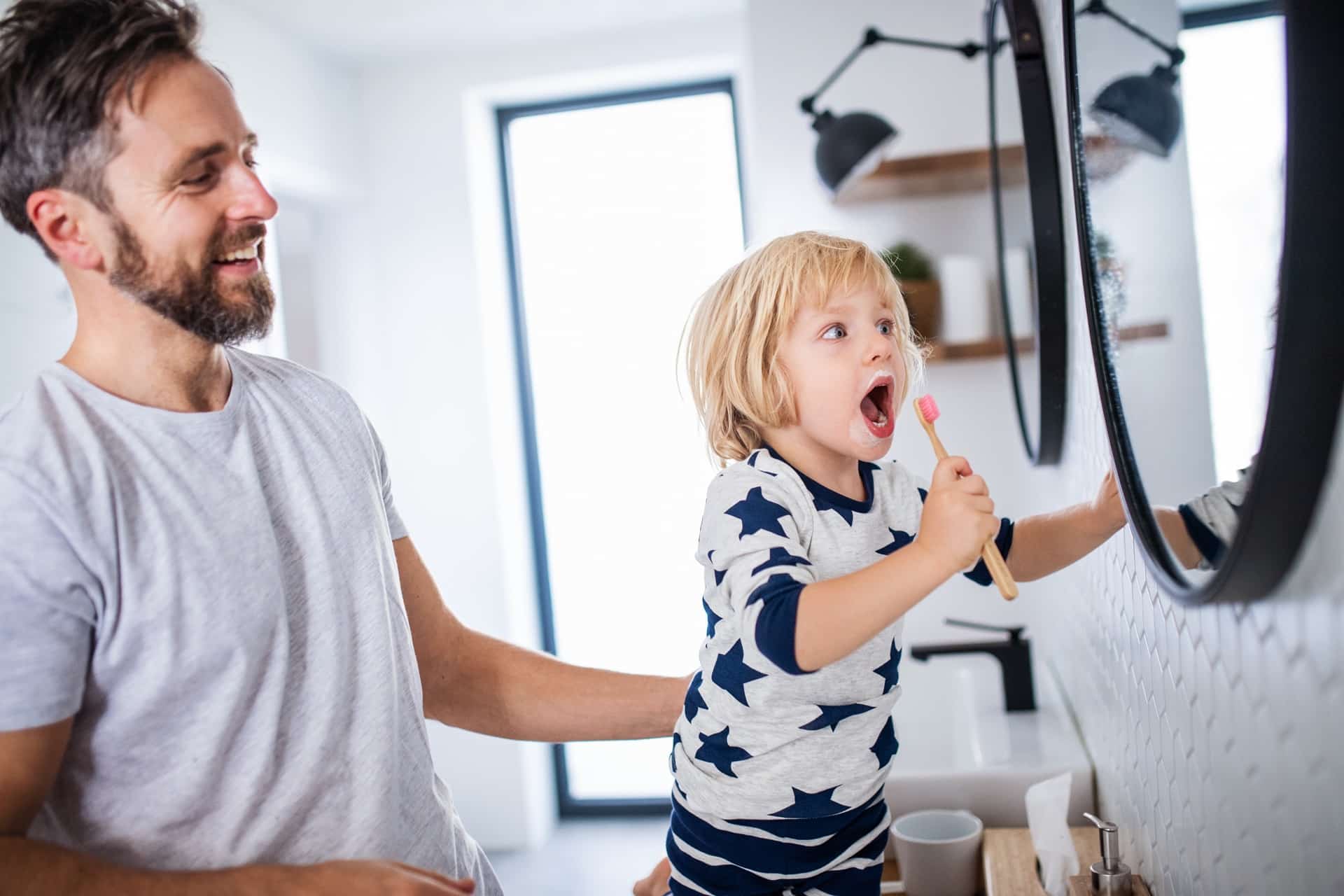 mature father with small son indoors in bathroom, brushing teeth.