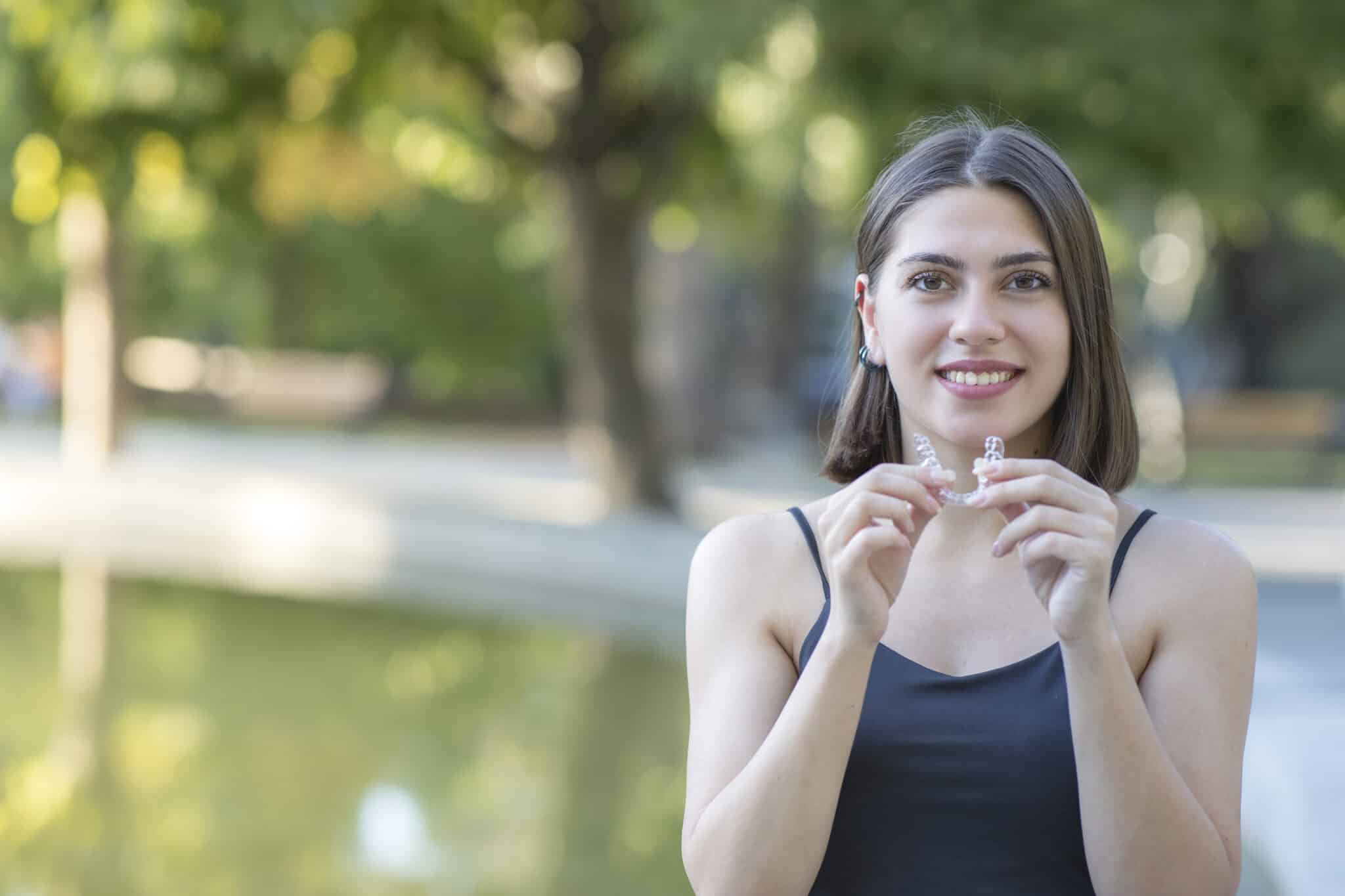 beautiful smiling woman is holding an invisalign brace