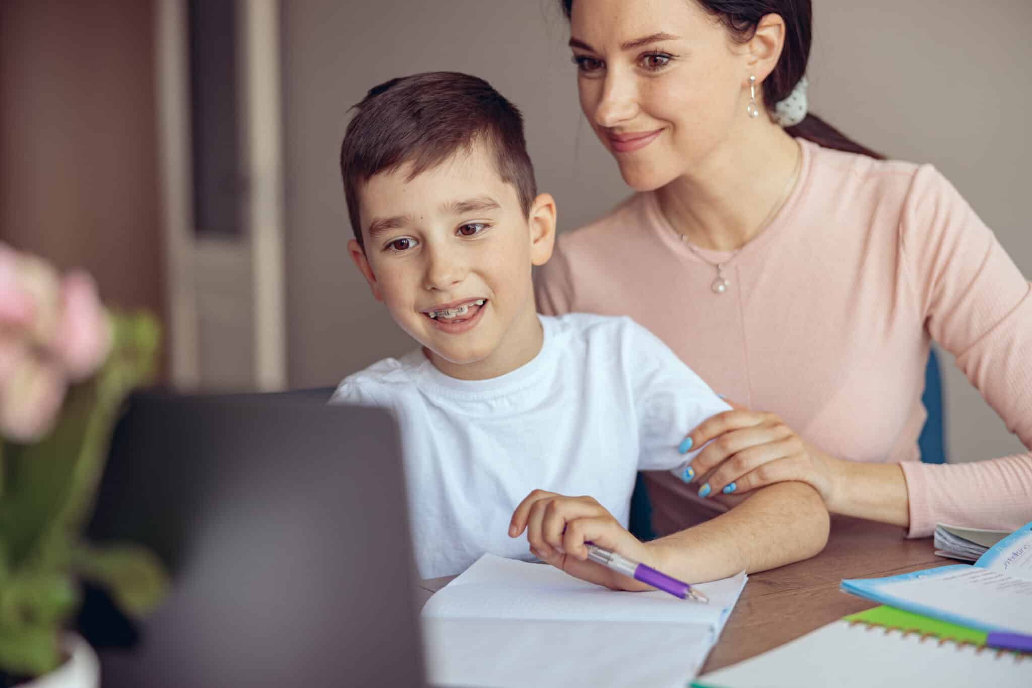 teen cute boy with braces learning homework at laptop computer and mom helping.