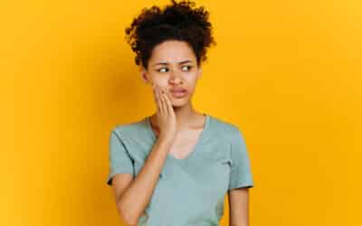 sad unhealthy african american woman touching her cheek with hand with painful expression because of toothache or dental illness on teeth, standing on orange isolated background. toothache concept