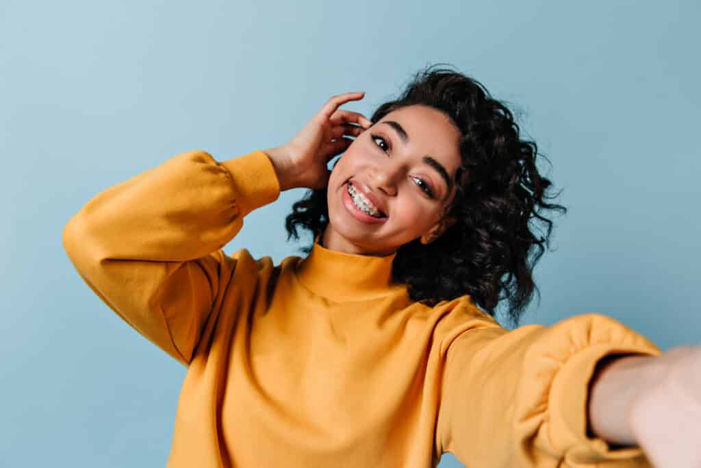 Pleased girl in dental braces taking selfie. Studio shot of gorgeous woman in yellow sweatshirt pleased girl in dental braces taking selfie. studio shot of gorgeous woman in yellow sweatshirt