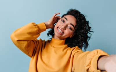 pleased girl in dental braces taking selfie. studio shot of gorgeous woman in yellow sweatshirt