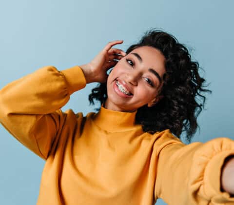 pleased girl in dental braces taking selfie. studio shot of gorgeous woman in yellow sweatshirt