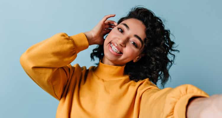 pleased girl in dental braces taking selfie. studio shot of gorgeous woman in yellow sweatshirt